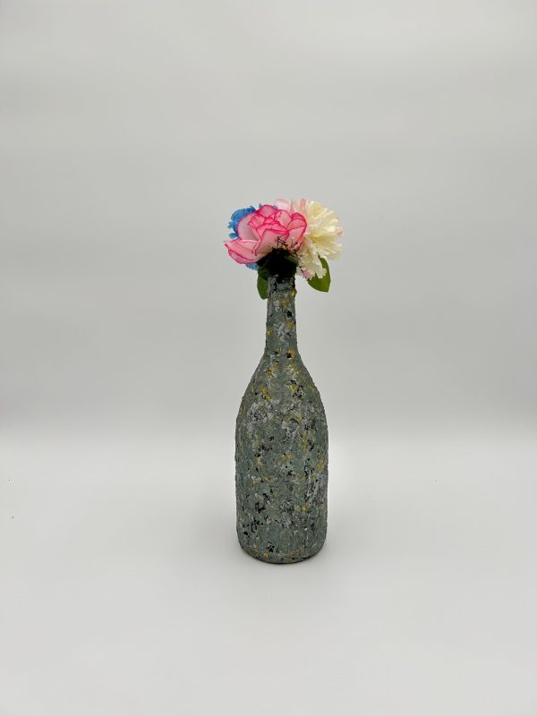 Olive green vase hand painted with tiny black and white spots with floral arrangement inside.