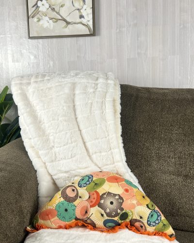 Orange throw pillow handmade into umbrella shape sitting on sofa and blanket