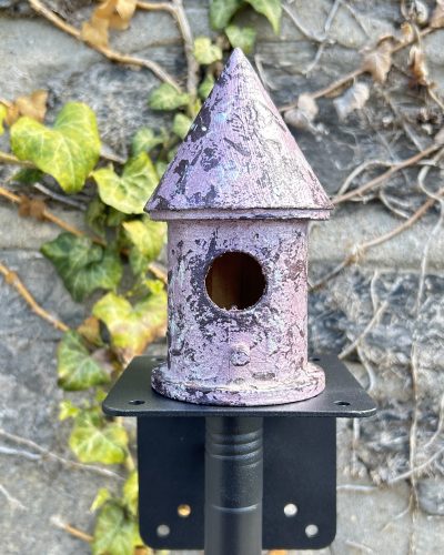 Hand painted purple birdhouse outside on garden pole in yard