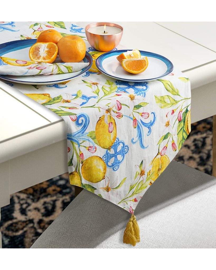 Handmade white, blue and yellow table runner with fruit sitting on it.